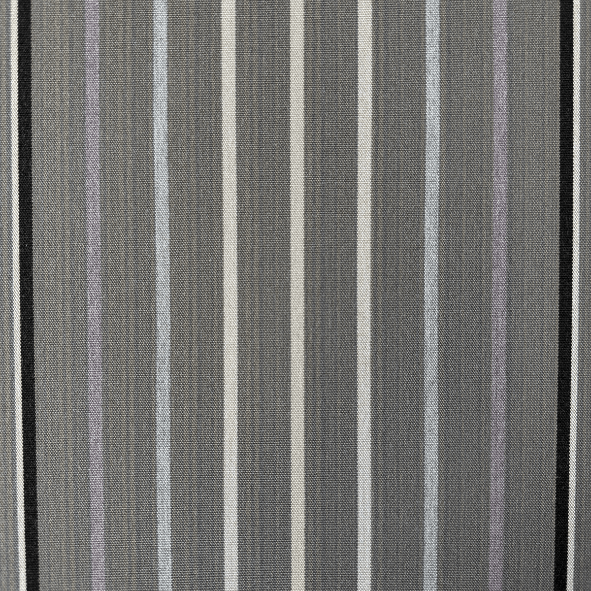 A close-up of a sunbrella motive striped canvas pattern featuring vertical stripes in charcoal gray, black, off-white, light blue-gray, and muted lavender.