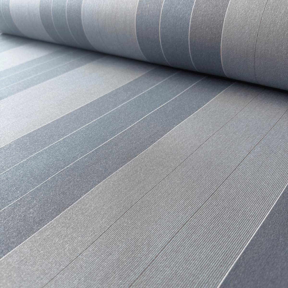 A close-up of a rolled piece of canvas fabric with a striped pattern in shades of gray and blue-gray, showing a fine ribbed texture.